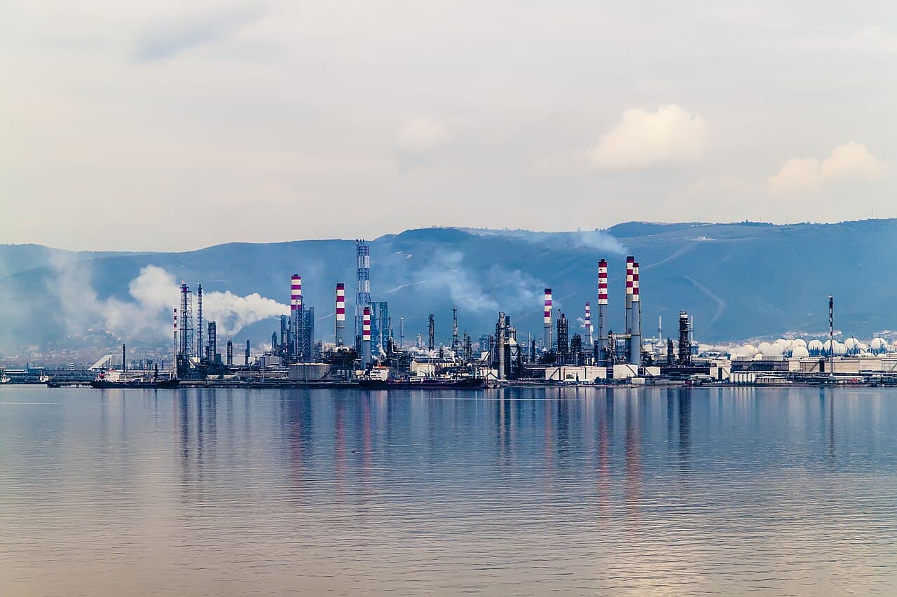 A large oil and natural-gas refinery beside calm water, representing the energy and refining groups leading a risk-off U.S. market